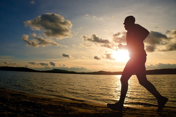 Entraînement au coucher du soleil. Une silhouette de jogger sur le chemin le long de la côte du lac
. - Photo, image