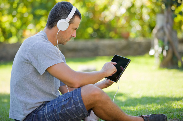 молодой человек отдыхает с планшетным компьютером, слушая музыку в наушниках
 - Фото, изображение