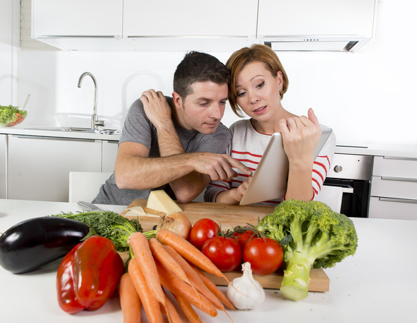 amerikanisches Paar in der heimischen Küche Frau nach Rezept in digitalem Block arbeiten zusammen mit Ehemann  - Foto, Bild