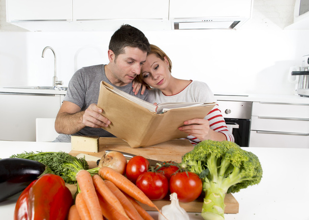 Pareja estadounidense trabajando en la cocina doméstica siguiendo la receta de lectura libro de cocina juntos
  - Foto, Imagen