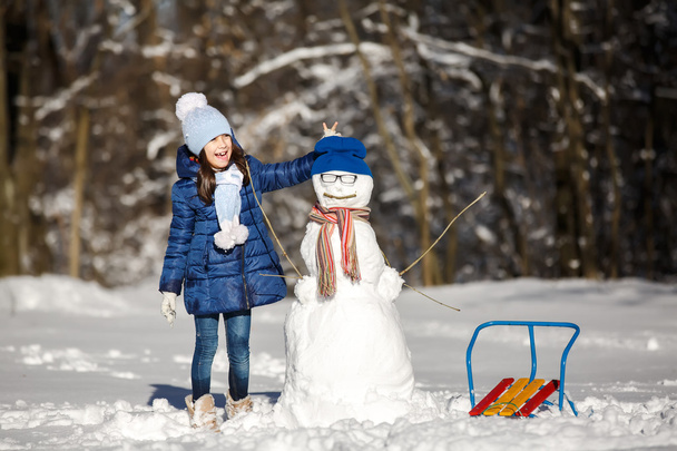 小さな女の子が雪だるまで遊んで - 写真・画像