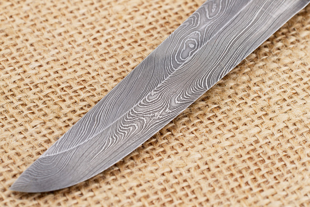 Frammento della tradizionale lama del coltello finlandese fatta a mano con il motivo astratto a onde di acciaio damasco su un vecchio sfondo a sacco
. - Foto, immagini