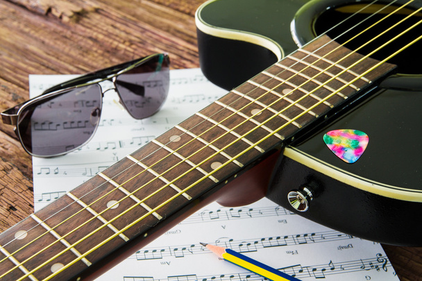 Akusztikus gitár, napszemüveg és lap kották az asztalon - Fotó, kép