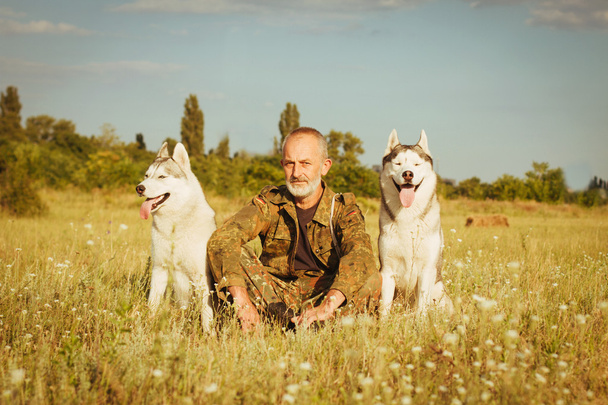 Viejo con barba sentado en un pajar con sus perros, disfrutando del atardecer de verano
. - Foto, imagen