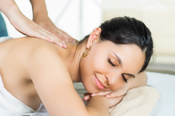 Modèle brune hispanique obtenir un traitement de spa de massage, serviette blanche couvrant le haut du corps couché horizontal souriant à la caméra
 - Photo, image