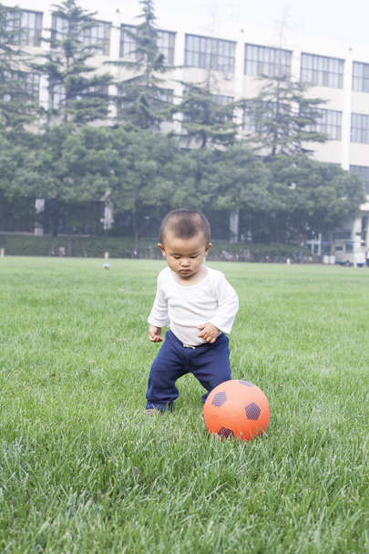Lindo niño chino jugando fútbol en el prado
 - Foto, Imagen