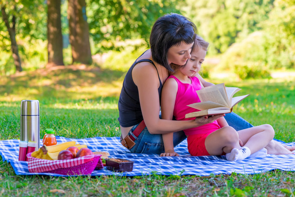 Mom and daughter reading a book on the lawn in the park - Фото, изображение