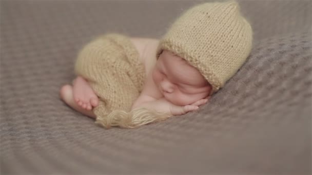 頭の下に手で素敵なポーズで毛布を横切る足の上に眠るニットキャップで愛らしい小さな新生児のクローズアップ。シーケンス内の 2 つのショット - 映像、動画