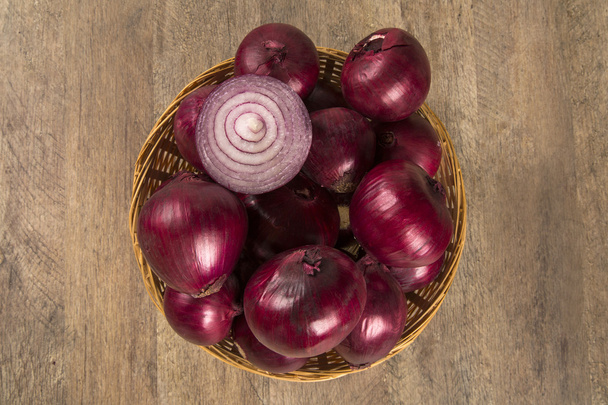 Red onions in a basket and a cut red onion over a table. - 写真・画像