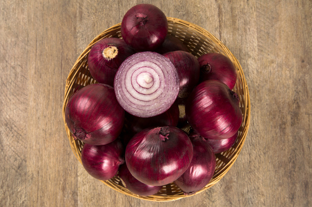 Red onions in a basket and a cut red onion over a table. - Zdjęcie, obraz