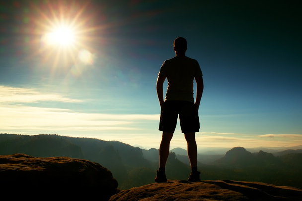 Seul randonneur en pantalon noir debout sur l'empire rocheux et veiller sur la vallée du matin brumeux et brumeux au soleil
. - Photo, image