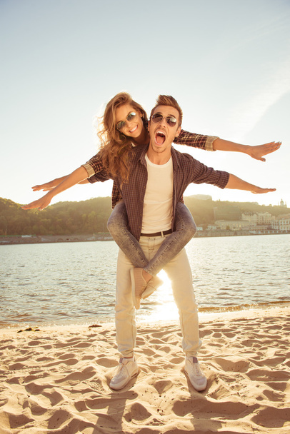 Happy young man piggybacking his girlfriend at the seaside - Foto, Bild