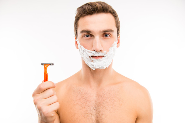 Pretty young man with shaving foam on his cheeks holding a razor - Zdjęcie, obraz