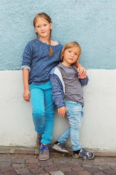 Deux enfants, fille et petit garçon, posant dehors, debout contre un mur bleu
 - Photo, image