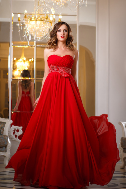 Beautiful young woman with perfect make up and hair style in gorgeous red evening dress in expensive luxury interior - Fotografie, Obrázek