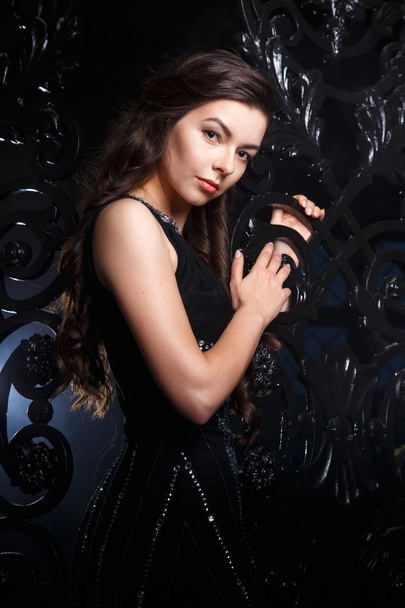 Portrait of elegant young brunette woman in black long evening dress in interior - Фото, изображение