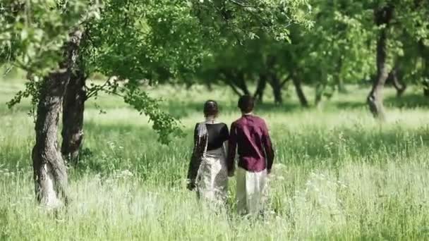 Młoda para kocha spacery trzymając ręce w letnim ogrodzie. Widok od tyłu - Materiał filmowy, wideo
