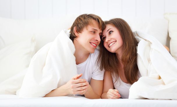 Щаслива пара сміється в ліжку, дивлячись з-під ковдри
 - Фото, зображення