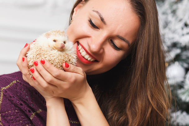Portrait of a girl in white clothes with a little hedgehog together over light christmas background - Photo, Image