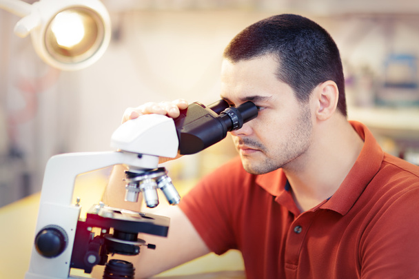 Νεαρό αρσενικό ερευνητή με μικροσκόπιο - Φωτογραφία, εικόνα
