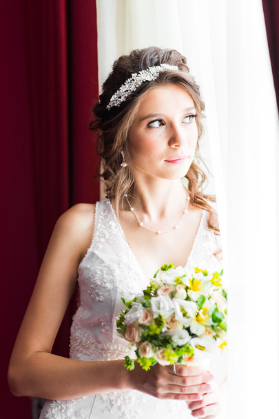 Beautiful young bride with wedding makeup and hairstyle in bedroom - Foto, afbeelding