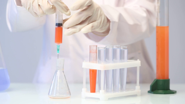 química femenina vertiendo un líquido rojo en un matraz químico
. - Imágenes, Vídeo