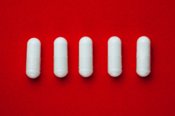білі капсули таблетки на червоному тлі
 - Фото, зображення