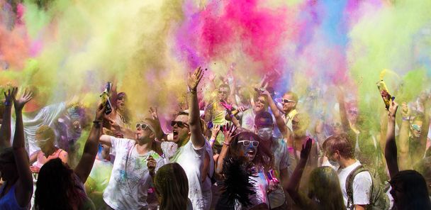 Велика група щасливих людей оточена рожевим і жовтим димом і порошком під час традиційного святкування Холі. - Фото, зображення