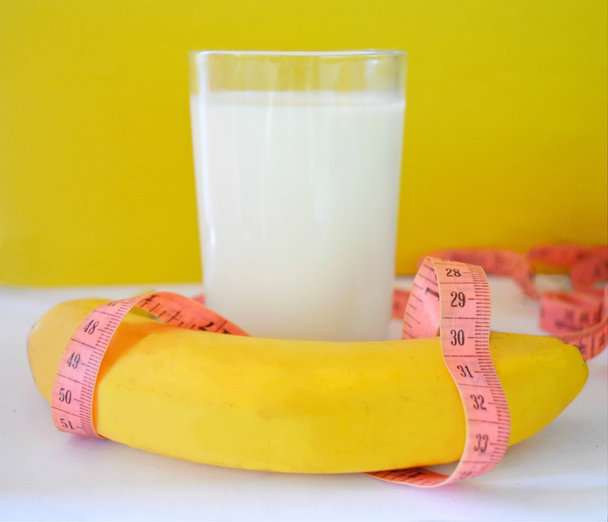 Szklanka mleka, banana i centymetrem na żółtym tle. Pojęcie diety - Zdjęcie, obraz