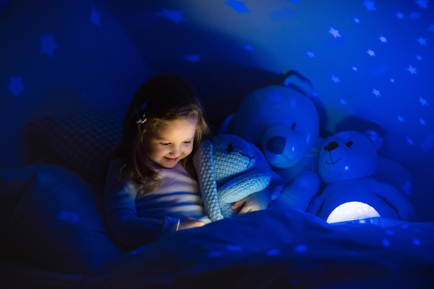Маленька дівчинка читає книжку в ліжку
 - Фото, зображення