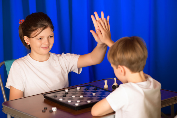 Діти хлопчика і дівчинки, які грають в настільну гру під назвою шашки - Фото, зображення