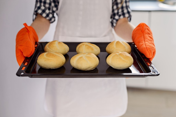жінка тримає піднос для випічки зі свіжоспеченими рулетами хліба
.  - Фото, зображення