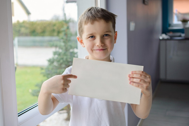 glücklicher Junge im Poloshirt, in der Hand ein leeres Blatt Papier - Foto, Bild