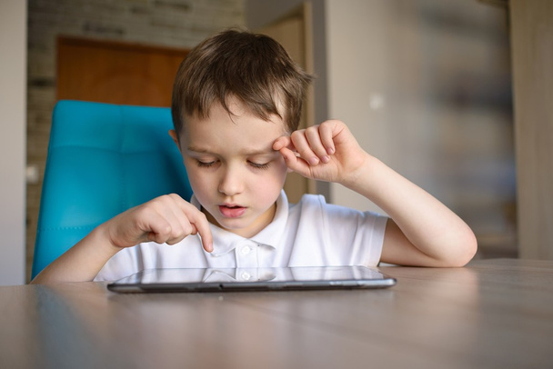  Niño de 6 años usando tableta mientras está sentado en la mesa.
 - Foto, imagen