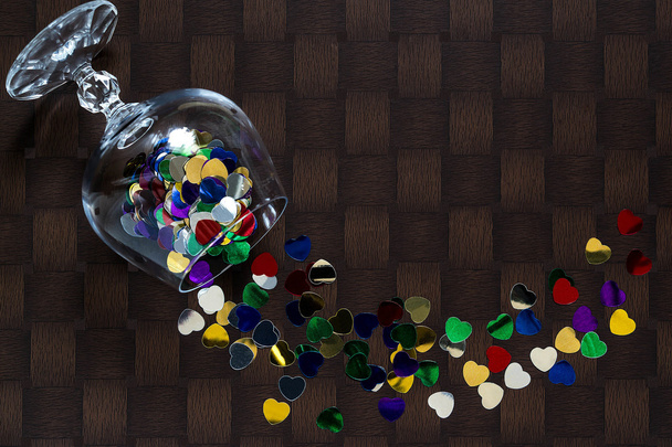 Brillante confeti en forma de corazón esparcida de una copa de vino
  - Foto, imagen