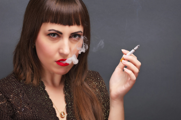 Gri bir arka plan üzerinde elinde sigara olan bir genç kadın - Fotoğraf, Görsel