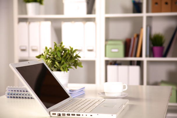 Κλείνω πάνω θέα του ένα εσωτερικό γραφείο εργασίας με έναν φορητό υπολογιστή, ένα φλιτζάνι καφέ και λευκό κουρτίνες σε μια ηλιόλουστη ημέρα - Φωτογραφία, εικόνα