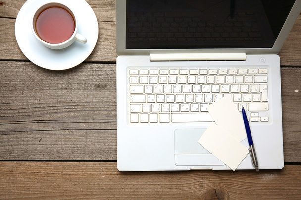 Lege visitekaartjes met pen, laptop en thee cup op houten office tabel - Foto, afbeelding