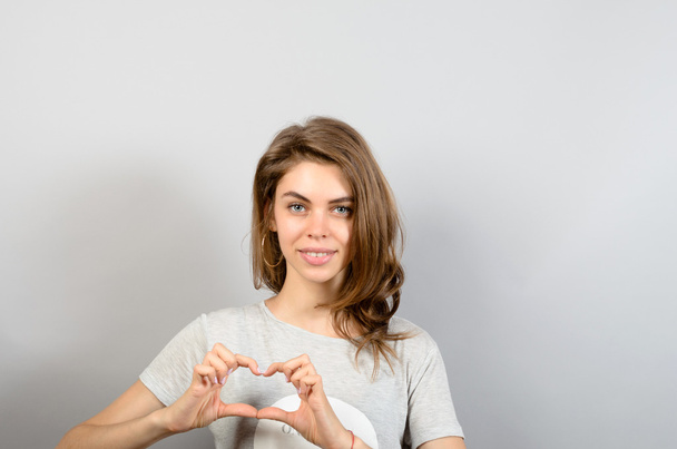Beautiful Woman Making Heart Shape Sign against grey background - 写真・画像