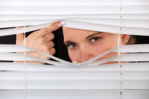 Curious woman peering through window blinds - Valokuva, kuva