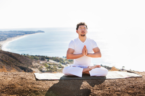 Hombre asiático medita en posición de yoga en altas montañas por encima del cielo azul
. - Foto, imagen