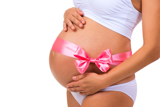 Close-up of pregnant belly with  pink ribbon bow for newborn baby girl. Concept of pregnancy. - Foto, immagini