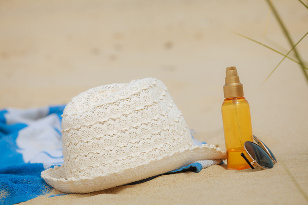 Beach set hat and sunscreen lotion lying on sand - Фото, изображение