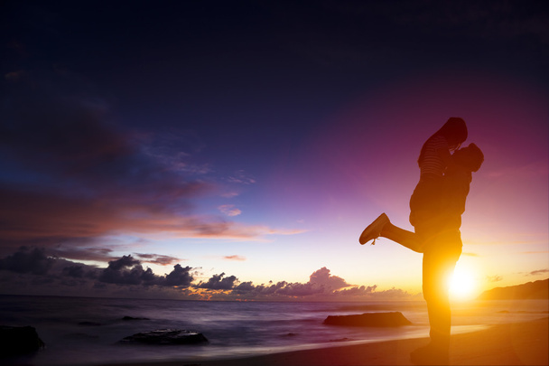 sunset silhouette of young couple in love hugging on beach - Foto, imagen