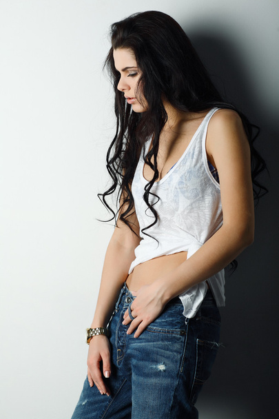 Portrait of beautiful sexual girl in jeans, standing near a white wall, in fashion style, glamur - Foto, afbeelding