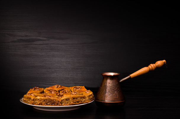 Cezve de café e um prato de baklava com mel em um fundo preto
 - Foto, Imagem