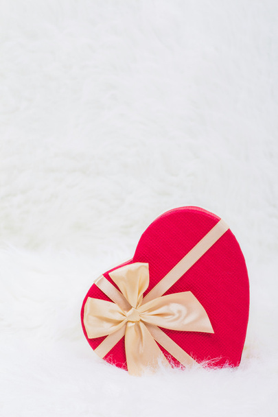 Red gift box in form of heart with beige bow on white furry back - Foto, Imagen