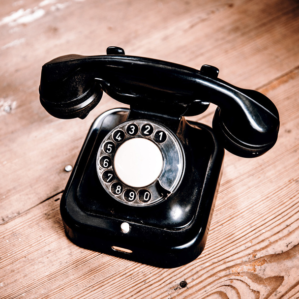 Vieux téléphone noir avec poussière et rayures sur le sol en bois
 - Photo, image