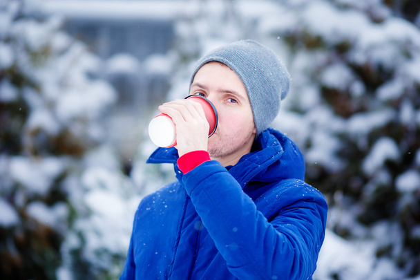 Nuori valkoihoinen mies juo kahvia jäätyneenä talvipäivänä ulkona
 - Valokuva, kuva
