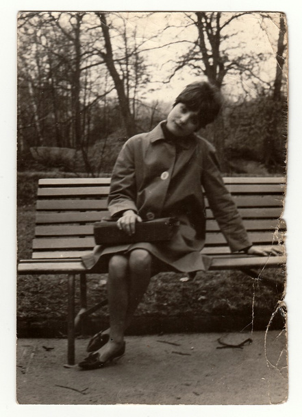 Vintage photo shows a young woman sit on a bench, circa 1960s. - 写真・画像